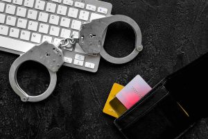 Arrest for stealing money online concept. Handcuff near keyboard and bank card on black background top view